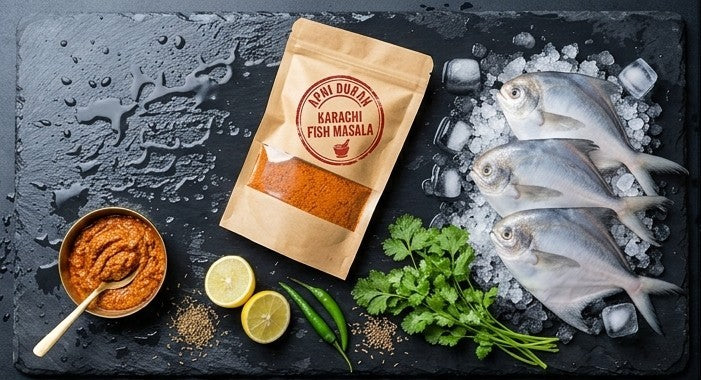 A top-down flat lay of whole spices and ingredients arranged around a central red circular logo reading 'APNI DUKAN'. Visible ingredients include ginger, turmeric, garlic cloves, red chilies, coriander seeds, cumin seeds, black peppercorns, cloves, and nuts on a dark textured surface.
